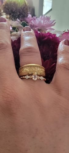 Reviewer's hand wearing the Elira ring stacked with another band. The delicate ring has a central stone and moissanite accents.