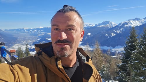 Reviewer in a caramel snow jacket, taking a selfie on a sunny, snowy mountain.