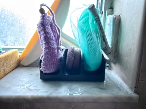 Reviewer's black Self Draining Soap Dish on a wet windowsill holding several soap bars and wash pouches.