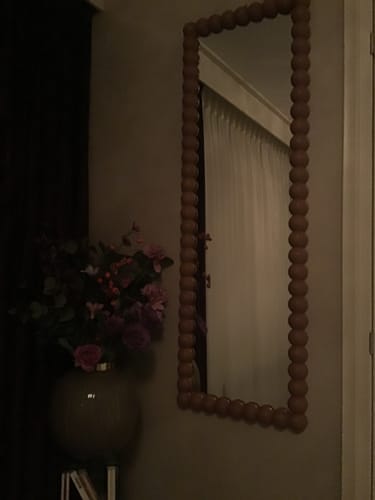 Recensent toont de Pompom spiegel hangend aan de muur in een sfeervol verlichte kamer.