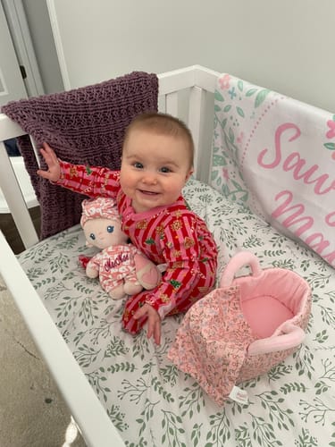 Reviewer's happy baby sitting in a crib with the Personalized Pudding Baby Girl doll.