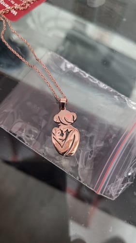 Customer's close-up of the rose gold Mom's Embrace Pendant on its link chain, resting on its packaging.