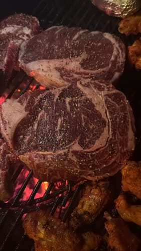 Primer plano del Rib Eye Steak de un cliente, sazonado y cocinándose sobre las brasas de una parrilla.