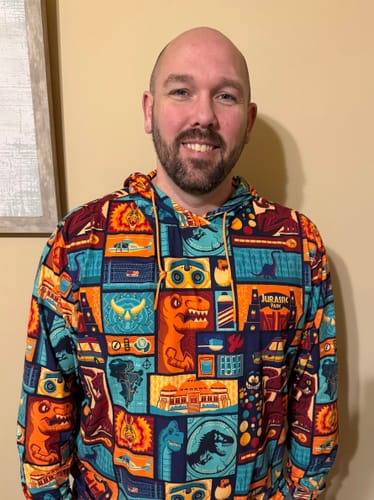 Reviewer smiling while wearing the colorful Jurassic Park 'Tiki Finds a Way' performance hoodie.