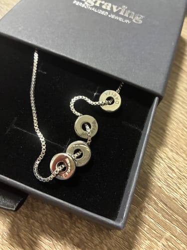 Customer's silver Orbit Necklace with several engraved ring pendants resting in a black jewelry box.