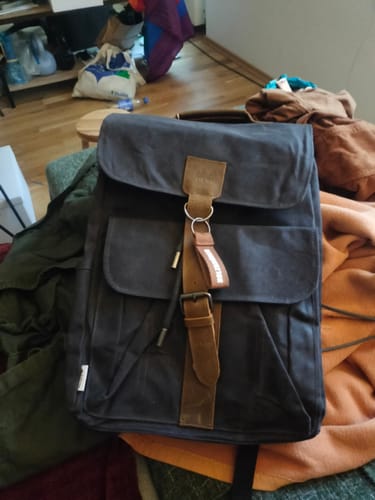 Kunde zeigt den dunklen Daypack Acadia - Natura mit braunen Riemen in einem Zimmer.