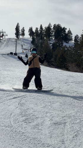 Reviewer snowboarding down a snowy slope wearing the baggy, coffee-colored waterproof snow pants.