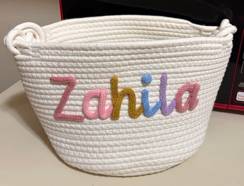 Customer's personalized white knitted basket with the name 'Zahila' written in multicolor yarn.