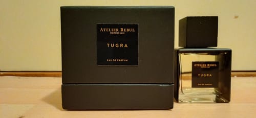 Recensent toont het Tugra Herenparfum flesje naast de zwarte doos op een houten oppervlak.