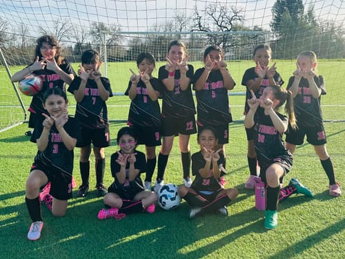 A customer's youth soccer team poses on a field wearing their custom black and neon pink soccer uniforms.
