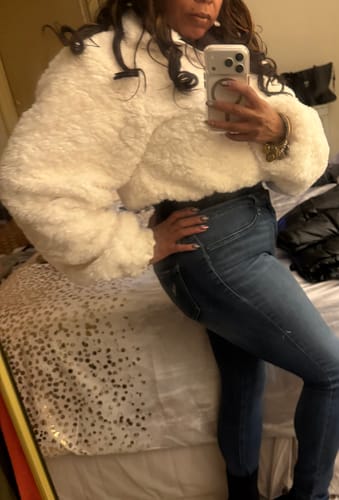 Reviewer wearing the white, fluffy Sherpa Quarter-Zip Cropped Sweater with dark jeans in a bedroom.