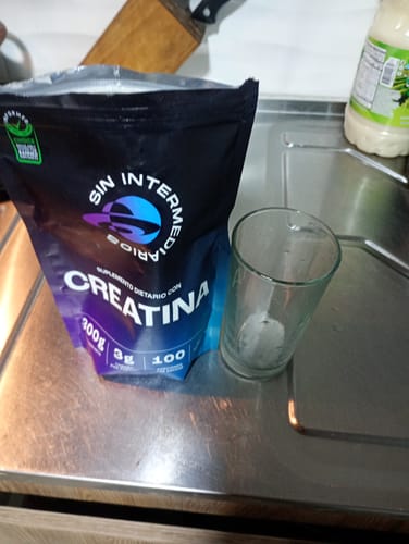 Empaque de la Creatina Monohidrato de un cliente sobre una encimera de cocina, junto a un vaso vacío.