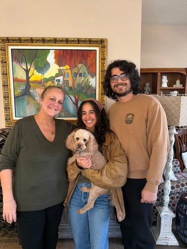 Customer wearing the Francesca Sweater in Pine Needle, standing indoors with two other people and a dog.