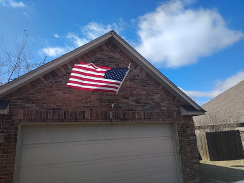 Customer's American flag wrapped around the flagpole on a brick house, showing the mounting rings not spinning freely.