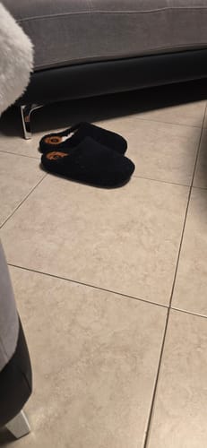 לקוח מציג זוג נעלי בית שחורות מדגם טדי על רצפת אריחים.