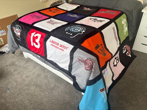 Customer's large Fuzz Monsta® T-Shirt Quilt with colorful shirt panels displayed across a bed.