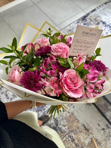Customer holds the lovely Spring Blossom Flower Bouquet with pink roses and magenta blooms.