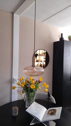 Recensent's Lucide Maloto hanglamp hangt boven een donkere eettafel met een boeket bloemen.
