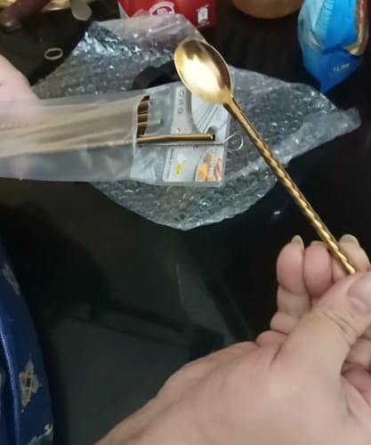 A customer holds a golden 2-in-1 Straw & Spoon with a textured handle, with the rest of the set in packaging in the background.