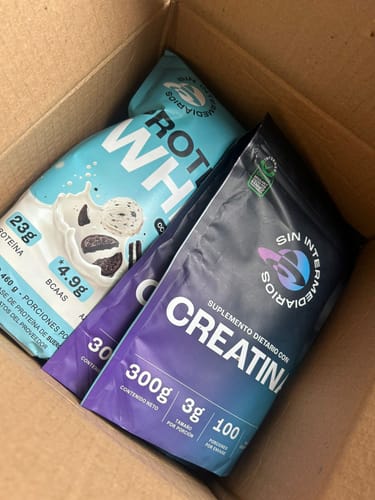 Un cliente muestra su Proteína Whey Cookies & Cream en una bolsa azul claro, dentro de una caja de envío.