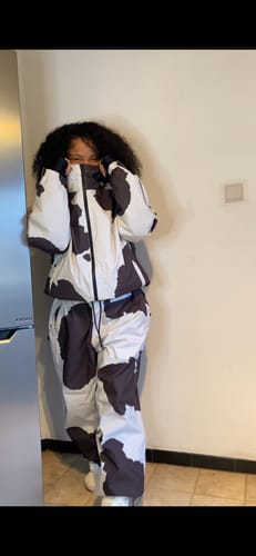 Reviewer wearing the baggy snow pants in a cow print, shown as part of a matching set.