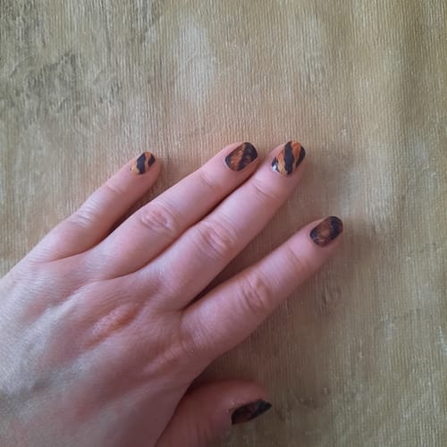 Hand einer Kundin, die Nagelfolien aus der Mystery Box mit einem orange-schwarzen Tigermuster trägt.