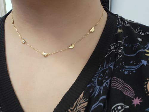 Customer wearing the gold Bubble Heart Multi Necklace, showing five small heart charms on a fine chain.