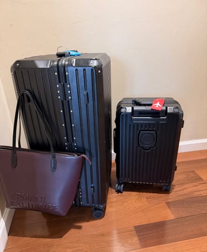 Customer's black Check-In Trunk Suitcase 30" and a matching smaller suitcase standing indoors on a wood floor.