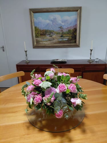Customer's Fabulous Rose Bowl with pink roses and greenery, shown as a centerpiece on a wooden dining table.