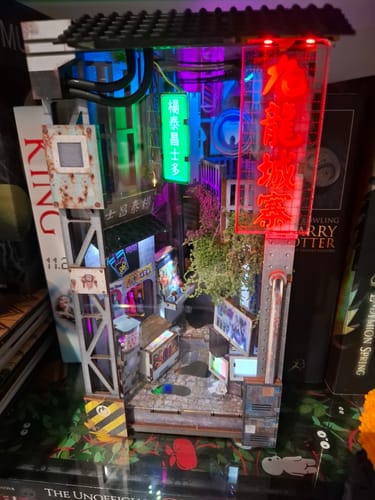 Customer's fully assembled Kowloon Walled City Book Nook Kit, displaying a detailed, lit-up cyberpunk alley on a bookshelf.