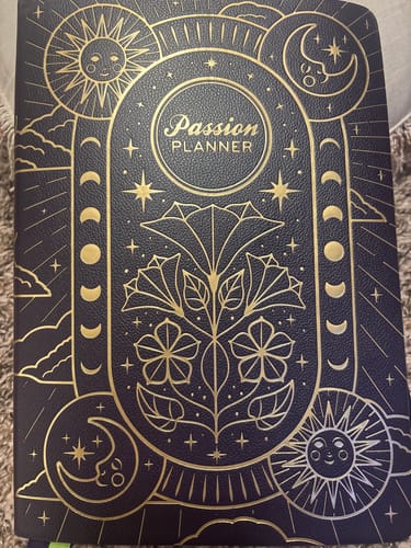 Customer's 'Cosmic Charm' weekly planner, showing the detailed gold foil celestial design on its dark cover.