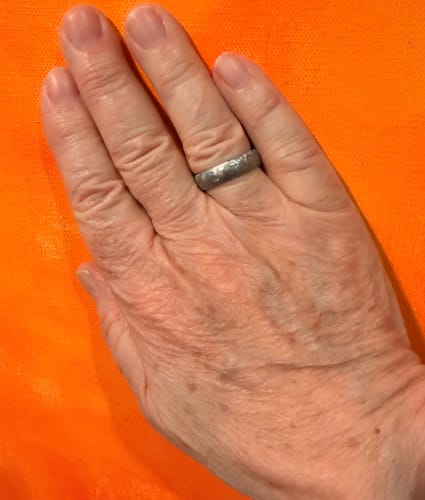 Reviewer's hand wearing the rugged Fjord ring, showcasing its hammered titanium texture against an orange background.
