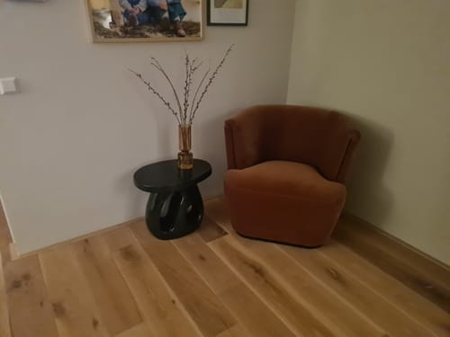 Klantfoto van de donkergroene Amé bijzettafel in een woonkamerhoek naast een fauteuil.