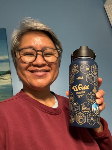 A happy customer holds up their dark blue Lets Wander™ World Explorer Water Bottle with one colorful sticker applied.