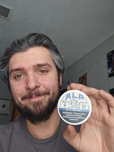 Reviewer smiling while holding up a round tin of Chilled Mint Nicotine Pouches.
