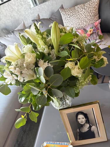 Customer's beautiful Elegant White Bouquet with lilies and greenery in a vase on a coffee table in a home setting.
