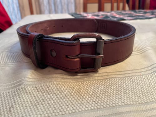 Customer's brown Gunner Stitched belt with the Distressed Bronze Roller Buckle, coiled on a table.