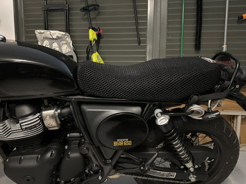 Close-up of a customer's black mesh Wind Rider Seat Cover fitted snugly on a motorcycle seat in a garage.