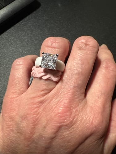 Customer's hand wearing the white Silicone Ring with a large princess-cut stone, stacked over a pink braided ring.