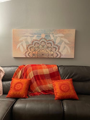 Customer's Boho Mandala Art V2 canvas hangs on a wall above a dark sofa with orange pillows.