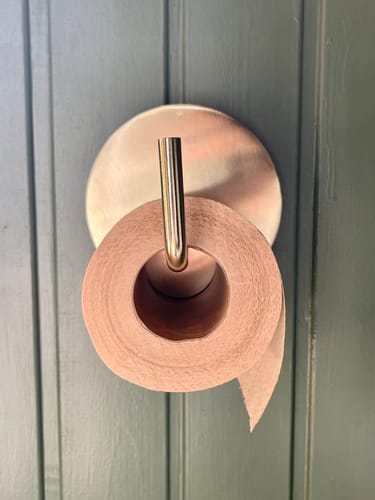 Reviewer's unbleached bamboo toilet paper on a stylish metal holder against a blue-grey wall.