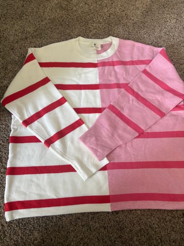 Reviewer's two-tone striped sweater laid flat, showing one half with red stripes on white and the other half with pink stripes.