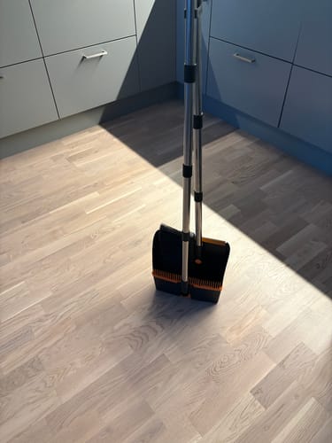 Anmelderens kost og støvbrett står sammenslått for oppbevaring på et lyst tregulv i et kjøkken.