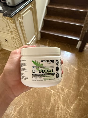 Customer holding a white tub of D-BLOAT powder in their home.
