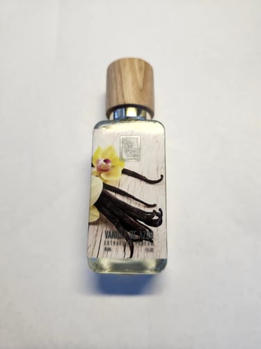 Reviewer's clear bottle of Vanille De Azur perfume with a wooden cap and vanilla-themed label on a white background.