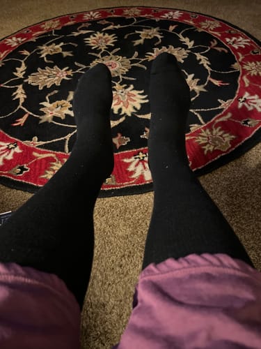 Customer wearing their black Performance Eucalyptus Compression Socks while resting their feet on a rug.
