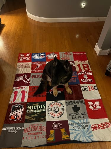 A customer's dog sits on their colorful Premium T-Shirt Quilt, which is spread out across a wood floor.