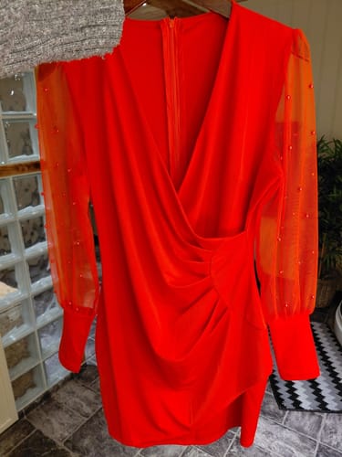 Rezensent zeigt das leuchtend rote, geraffte Kleid mit transparenten Ärmeln, die mit Perlen verziert sind.