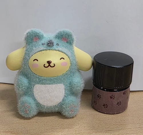 Customer's bottle of Cheeky Gremlin perfume with a paw-print label next to a small, fuzzy character toy.