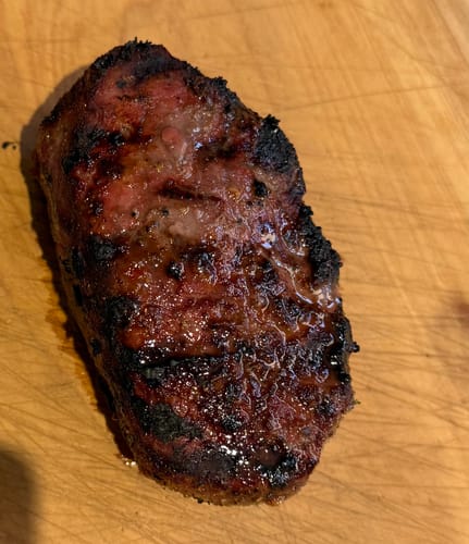 Customer's grilled USDA Prime Top Sirloin with a dark char on a wooden cutting board.